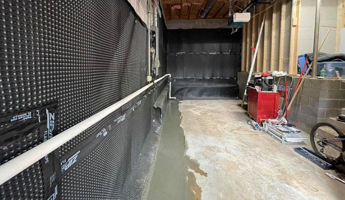 An unfinished basement showing the walls covered with black dimpled waterproofing membrane