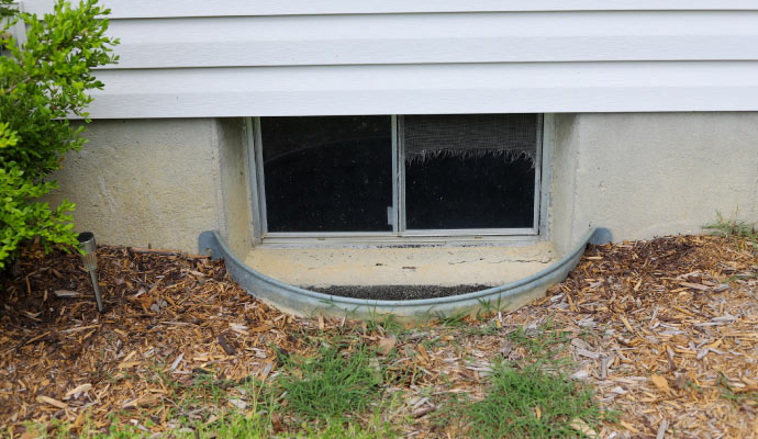 A basement window with a metal grate well covering