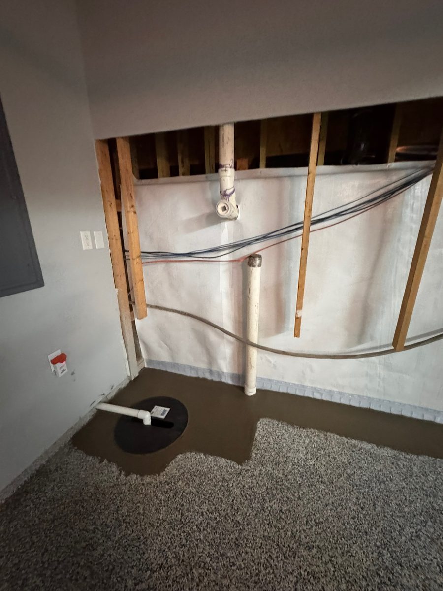 Installed sump pump basin and discharge lines along a finished basement wall