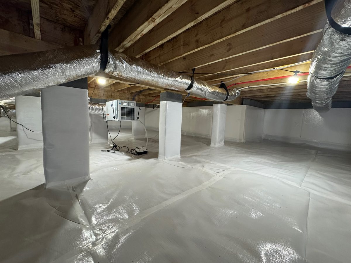 White vapor barrier covering the ground and support columns of a sealed crawl space