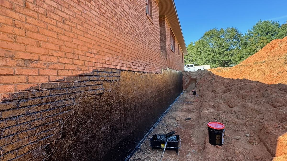 Exterior foundation wall coated with waterproofing membrane beside an open excavation trench
