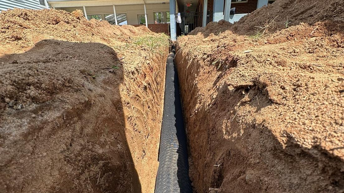 Exterior French drain trench and drain pipe alongside a foundation