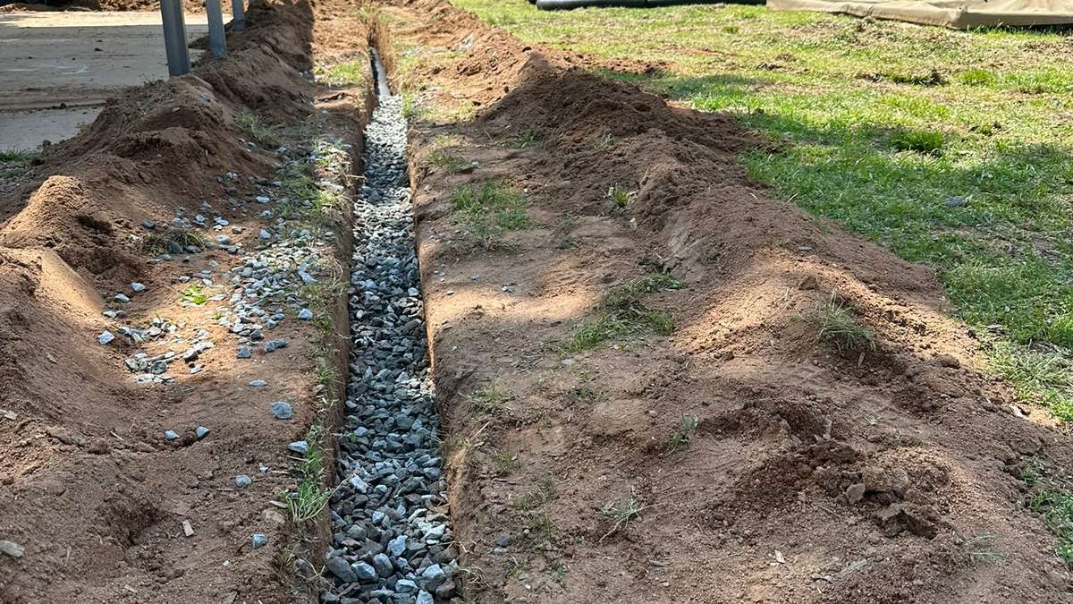 Completed gravel-filled exterior French drain running across a yard