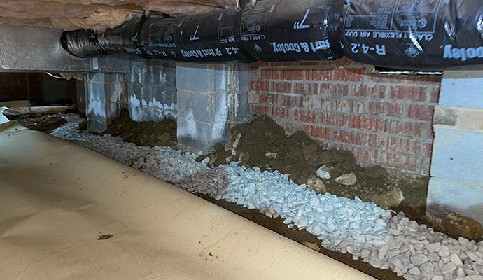 A gravel-filled perimeter drain being installed along the foundation wall of a crawl space.