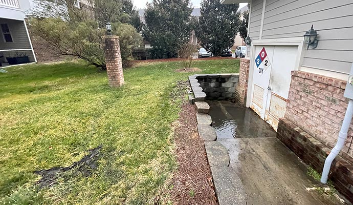 Waterlogged concrete walkway showing poor drainage next to a building foundation.